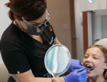 A young child in the dental chair holding a mirror