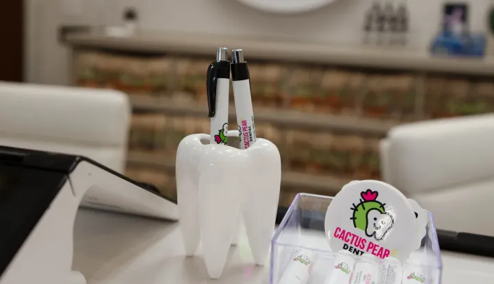 A tooth-shaped pen holder and Cactus Pear Dental cards on the front desk, the neon sign glowing behind