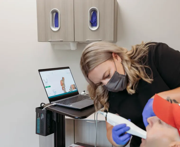 A Cactus Pear Dental clinician using an intraoral scanner, the 3D scan building on the laptop beside her